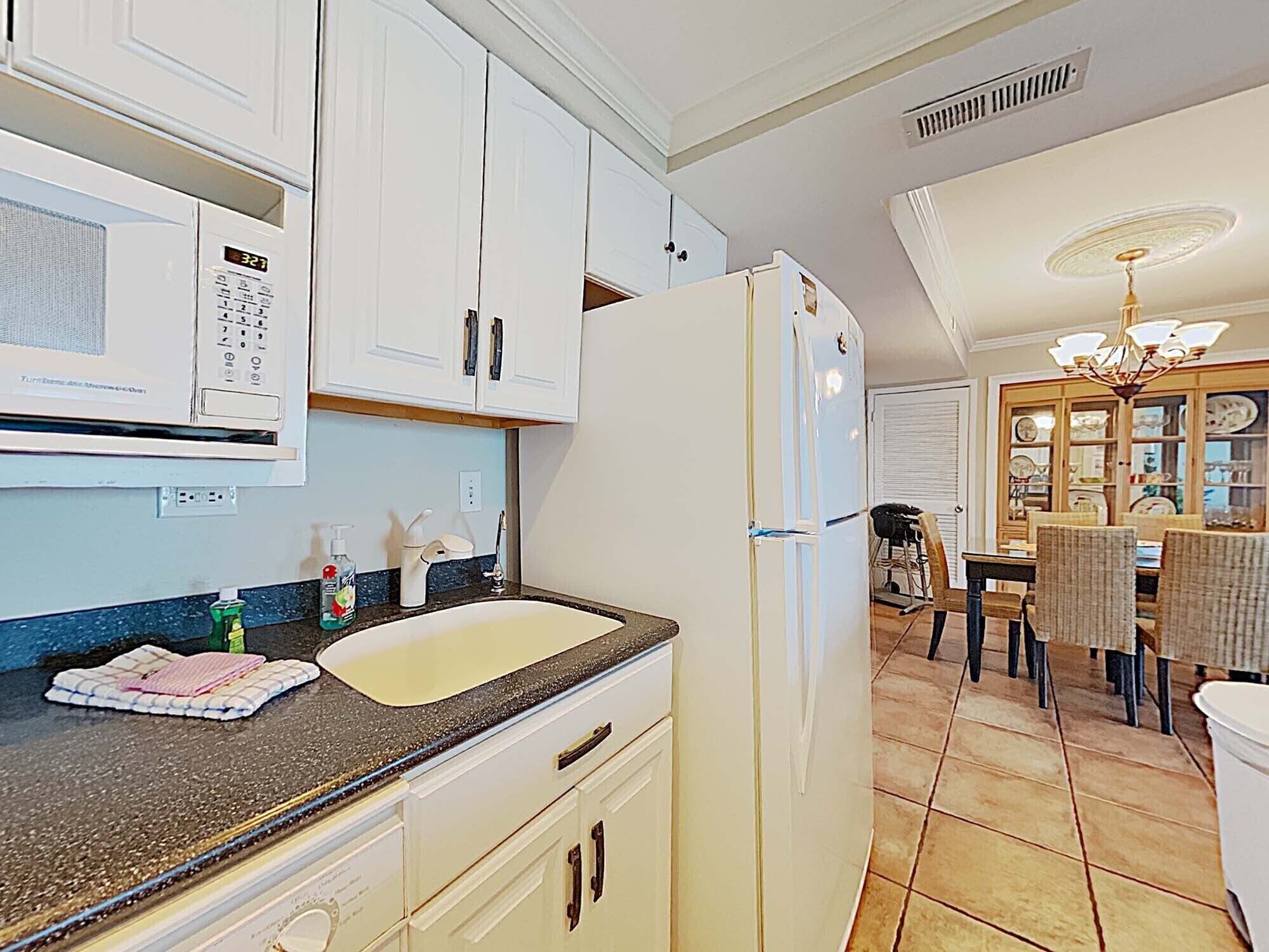 A kitchen with white cabinets, a microwave, a refrigerator, a sink, and a dining area with a chandelier.