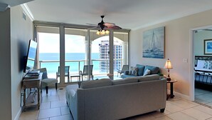 Un salon avec un canapé, un téléviseur et un balcon offrant une vue sur l’océan.