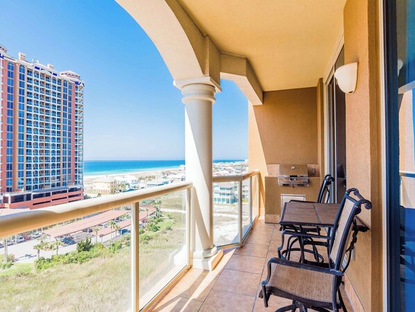 Un balcon avec vue sur la plage et l’océan, un barbecue et du mobilier d’extérieur.