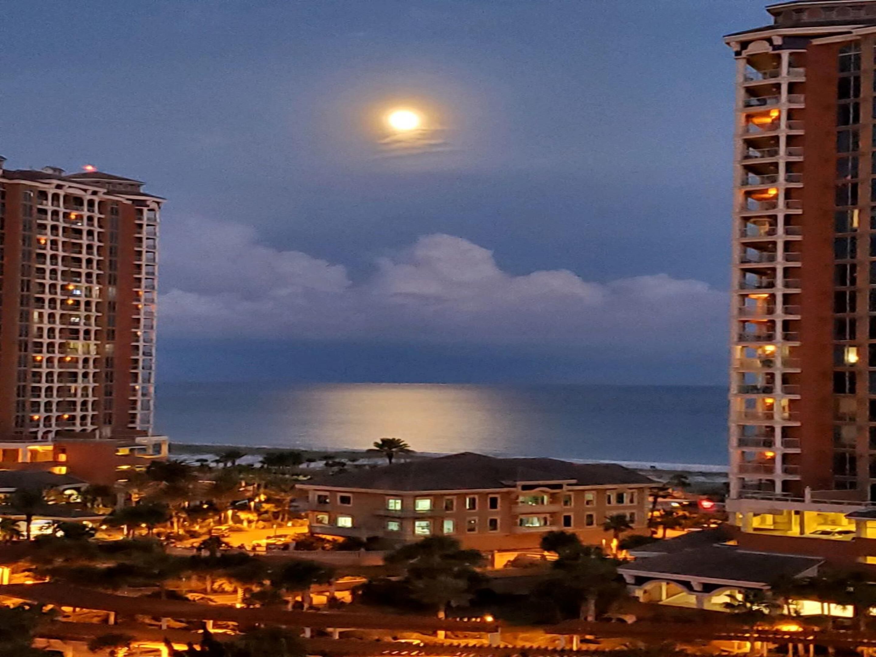 A coastal hotel with multiple floors, a view of the ocean, and a moon in the sky.