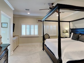 Una camera da letto con un letto a baldacchino, una ventola a soffitto e due finestre con tende.