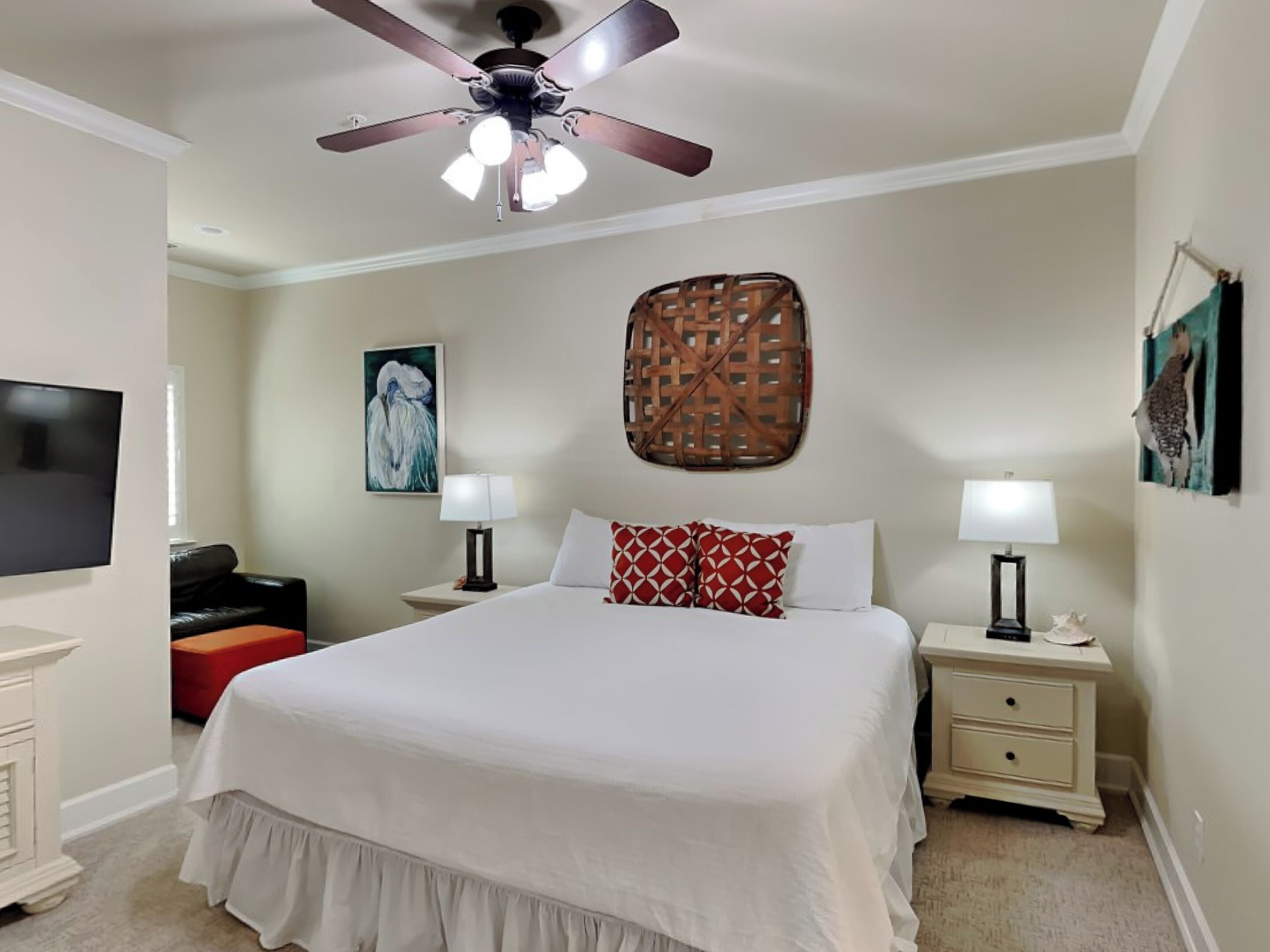 A hotel room with a large bed, two bedside tables with lamps, a ceiling fan, a flat-screen TV, and artwork on the walls.