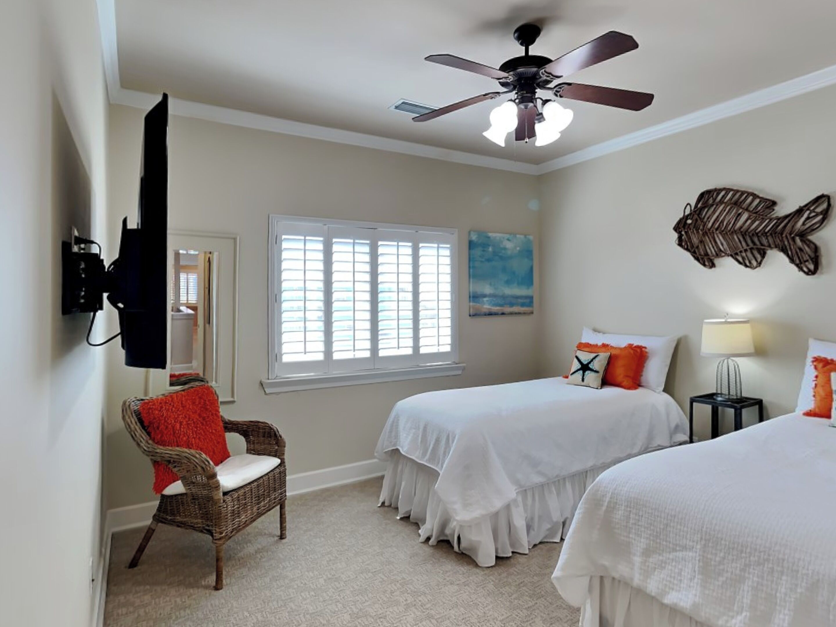 Une chambre avec deux lits, un ventilateur de plafond, une fenêtre avec des stores, un téléviseur fixé au mur et un tableau décoratif représentant des poissons.