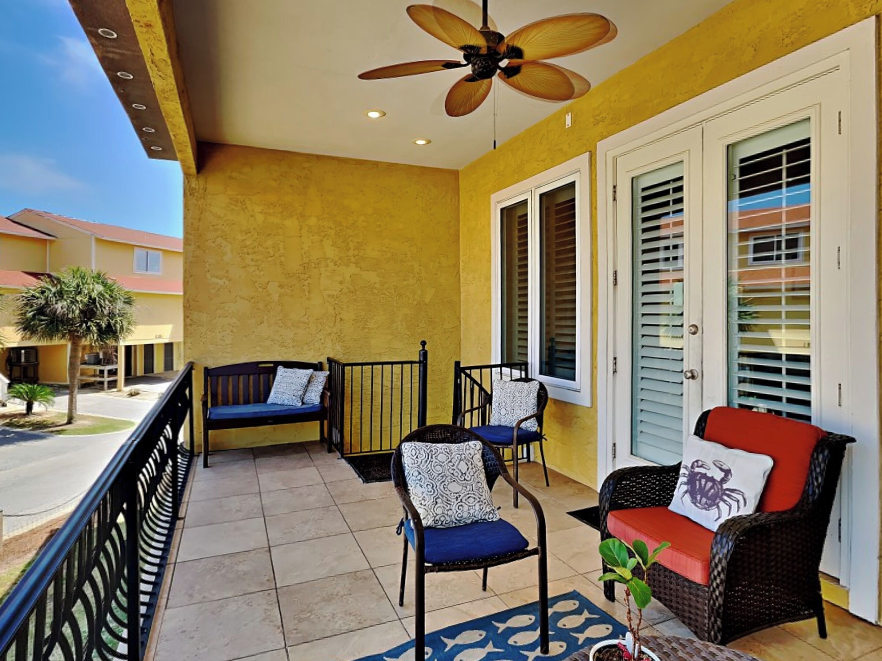 A balcony with a ceiling fan, two chairs, a bench, and a potted plant.