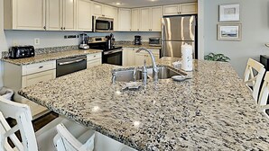 A modern kitchen with granite countertops, stainless steel appliances, and white cabinetry. - Regency Cabanas by Southern Vacation Rentals (Pensacola Beach)