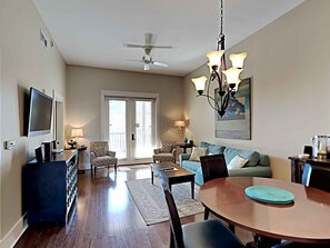A spacious living area with a dining table, two patterned armchairs, a sofa, a ceiling fan, and a chandelier.