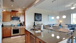 A modern kitchen with wooden cabinets, stainless steel appliances, and a large island with a sink. - Redfish Village by Southern Vacation Rentals (Santa Rosa Beach)