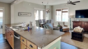 A spacious kitchen with a large island, a dining area with a table and chairs, a living room with a sofa and TV, and a ceiling fan. - Redfish Village by Southern Vacation Rentals (Santa Rosa Beach)