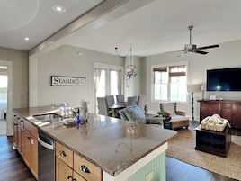 A spacious kitchen with a large island, a dining area with a table and chairs, a living room with a sofa and TV, and a ceiling fan.