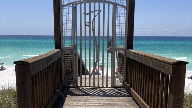 A wooden boardwalk leading to a beach with a metal gate and a view of the ocean. - Redfish Village by Southern Vacation Rentals (Santa Rosa Beach)