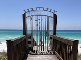 A wooden boardwalk leading to a beach with a metal gate and a view of the ocean.