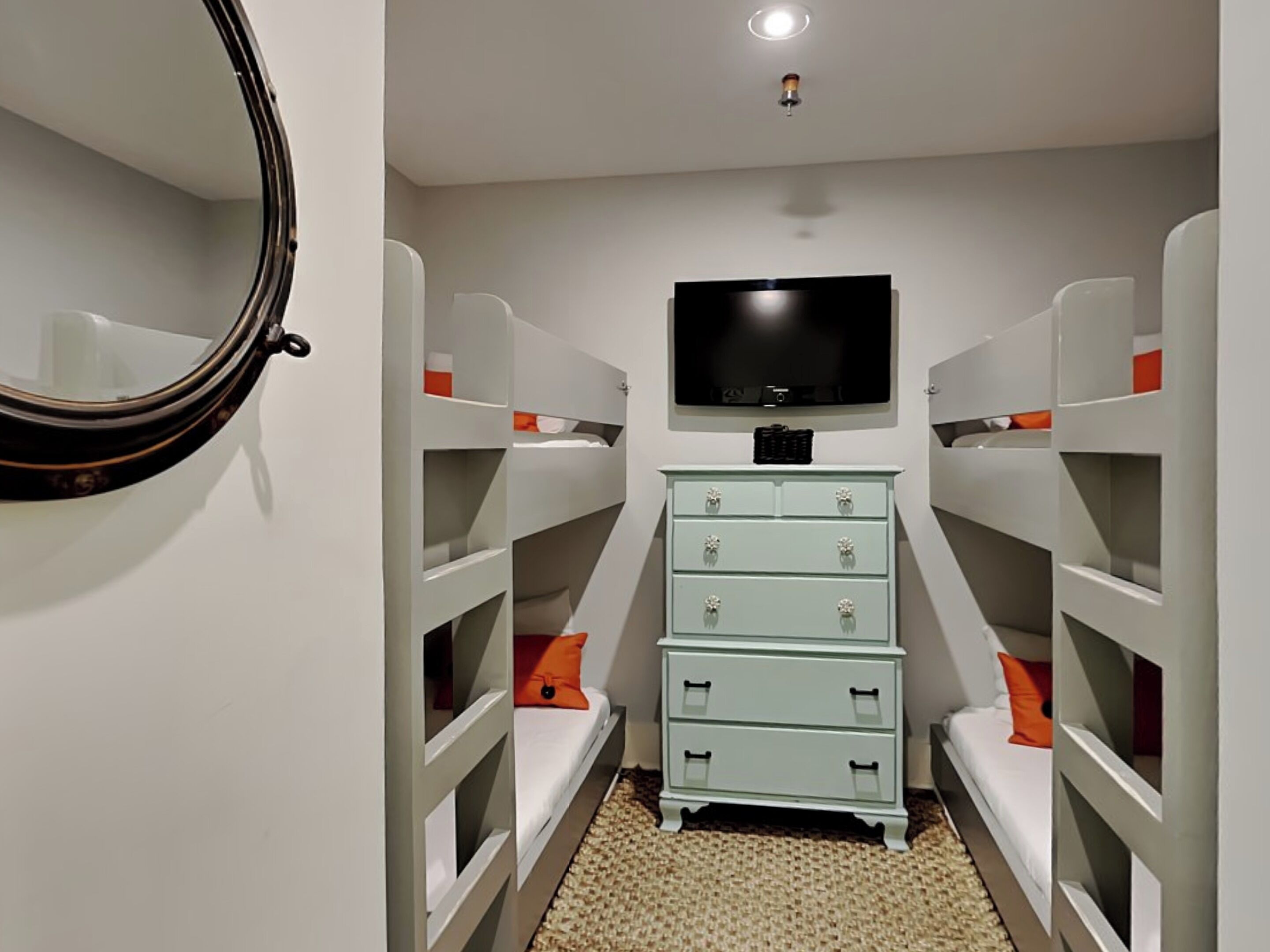 A bedroom with bunk beds, a dresser, a television, and a mirror.