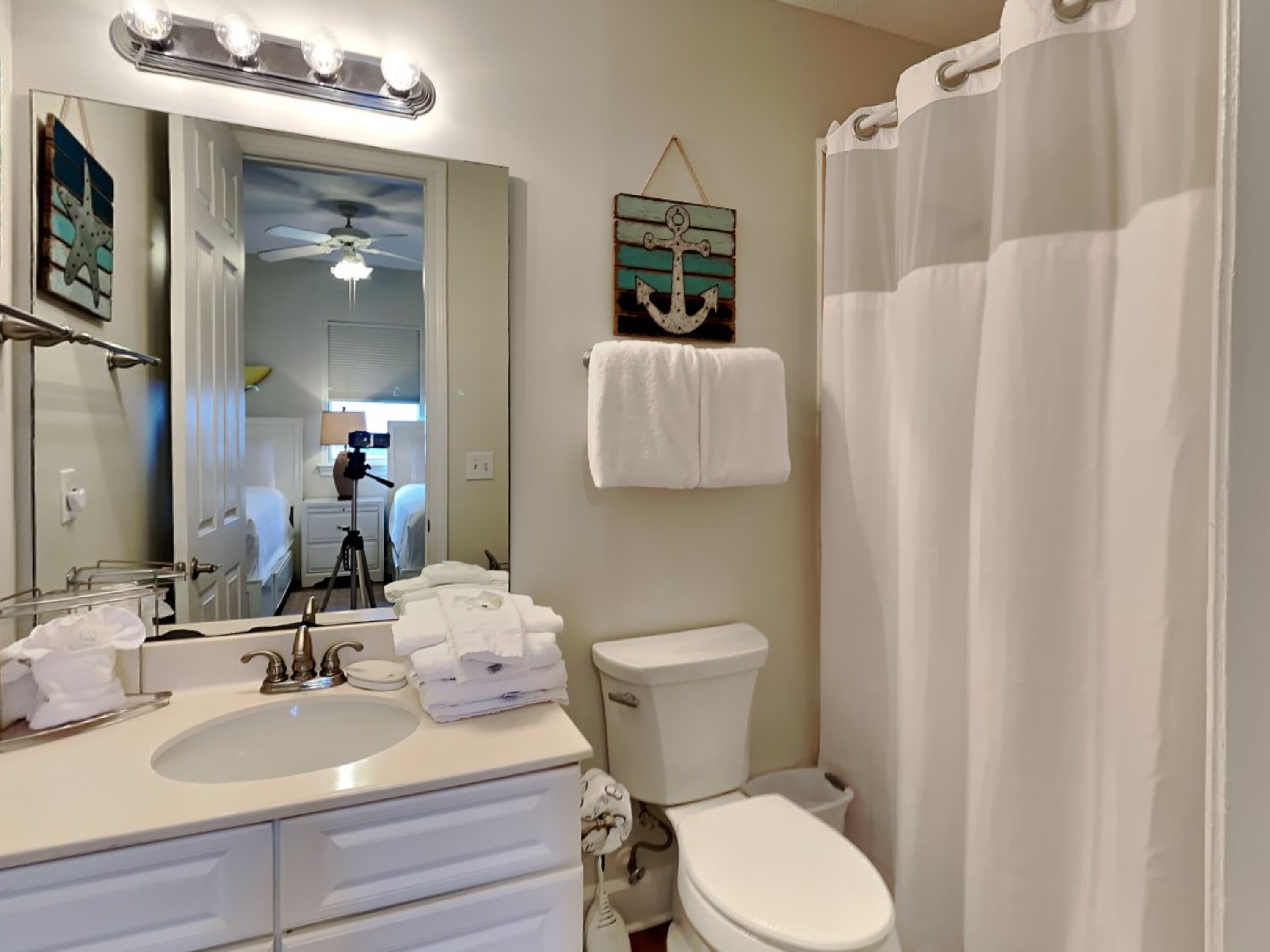 A bathroom with a sink, mirror, and toilet. There is a towel rack with towels and a decorative anchor.