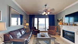 A living room with a leather sofa, two armchairs, a coffee table, a fireplace, and a large TV. - Regency Isle by Southern Vacation Rentals (Orange Beach)