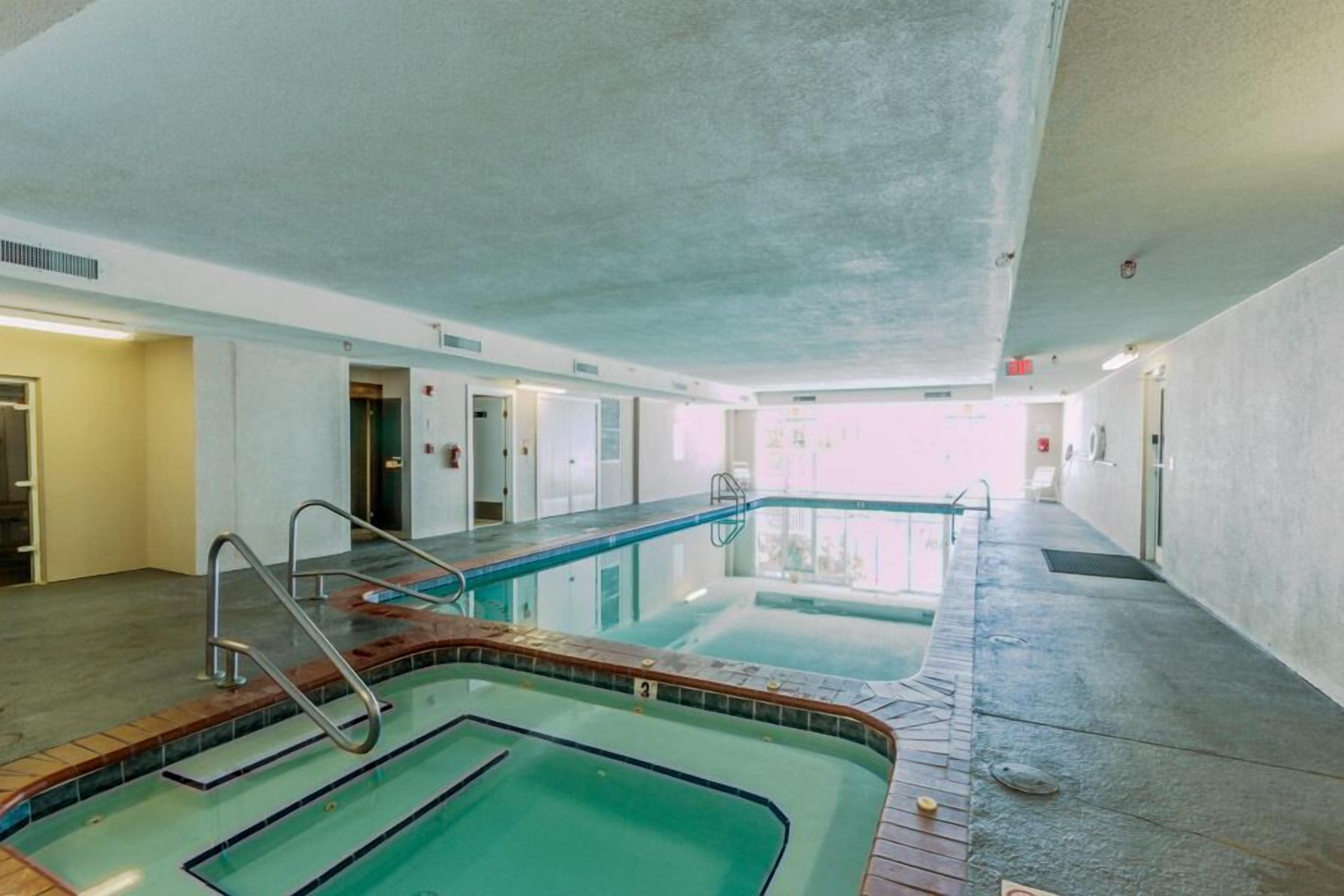An indoor swimming pool with clear water, a tiled deck, and a concrete ceiling.