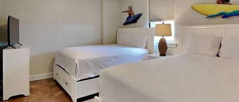Een hotelkamer met twee bedden, een plafondventilator, een televisie op een standaard en een raam met jaloezieën.