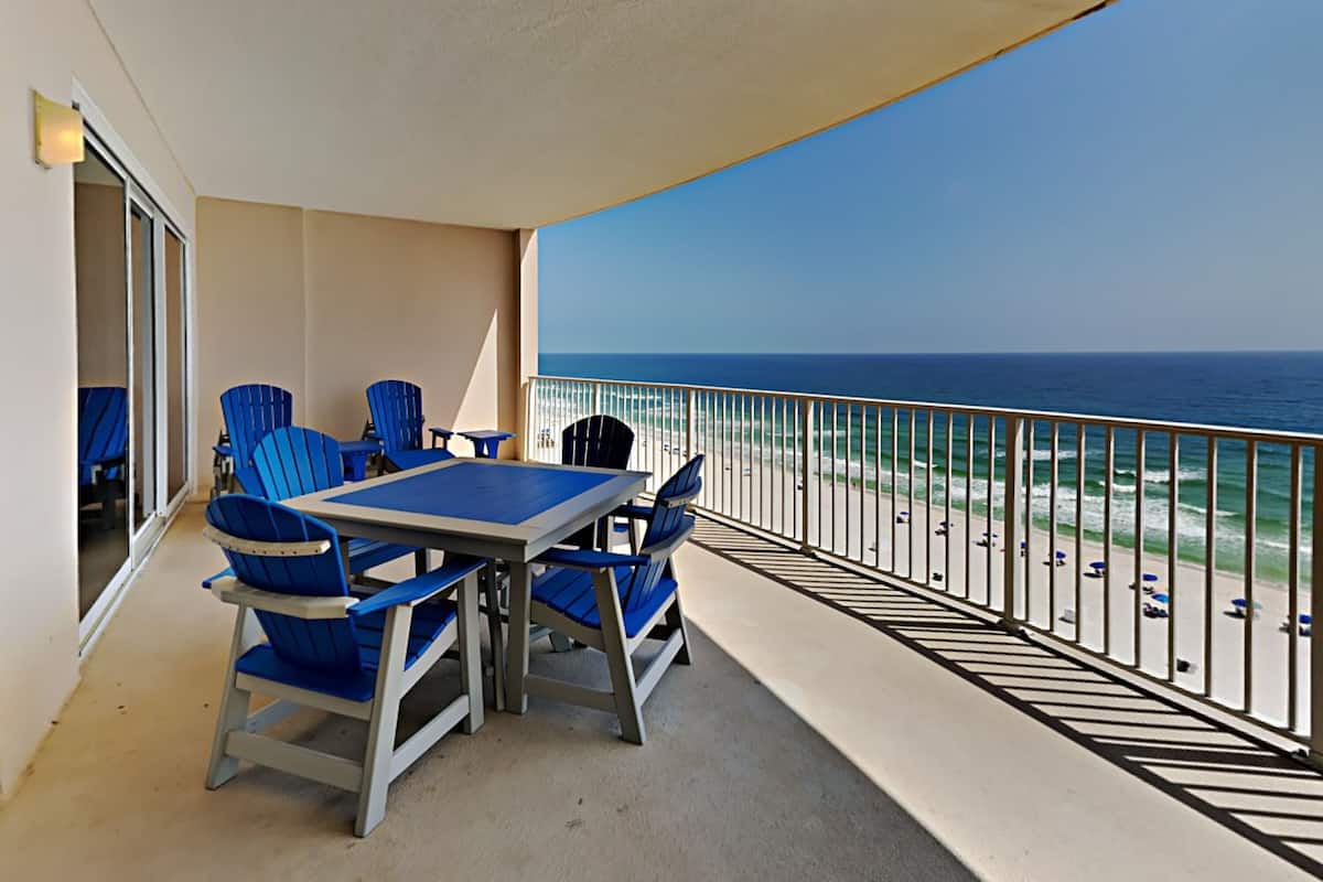 A balcony with a table and chairs, overlooking the beach and ocean.