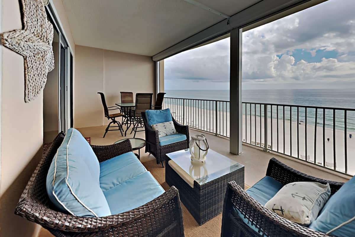A balcony with wicker furniture, a glass table, and a view of the ocean.