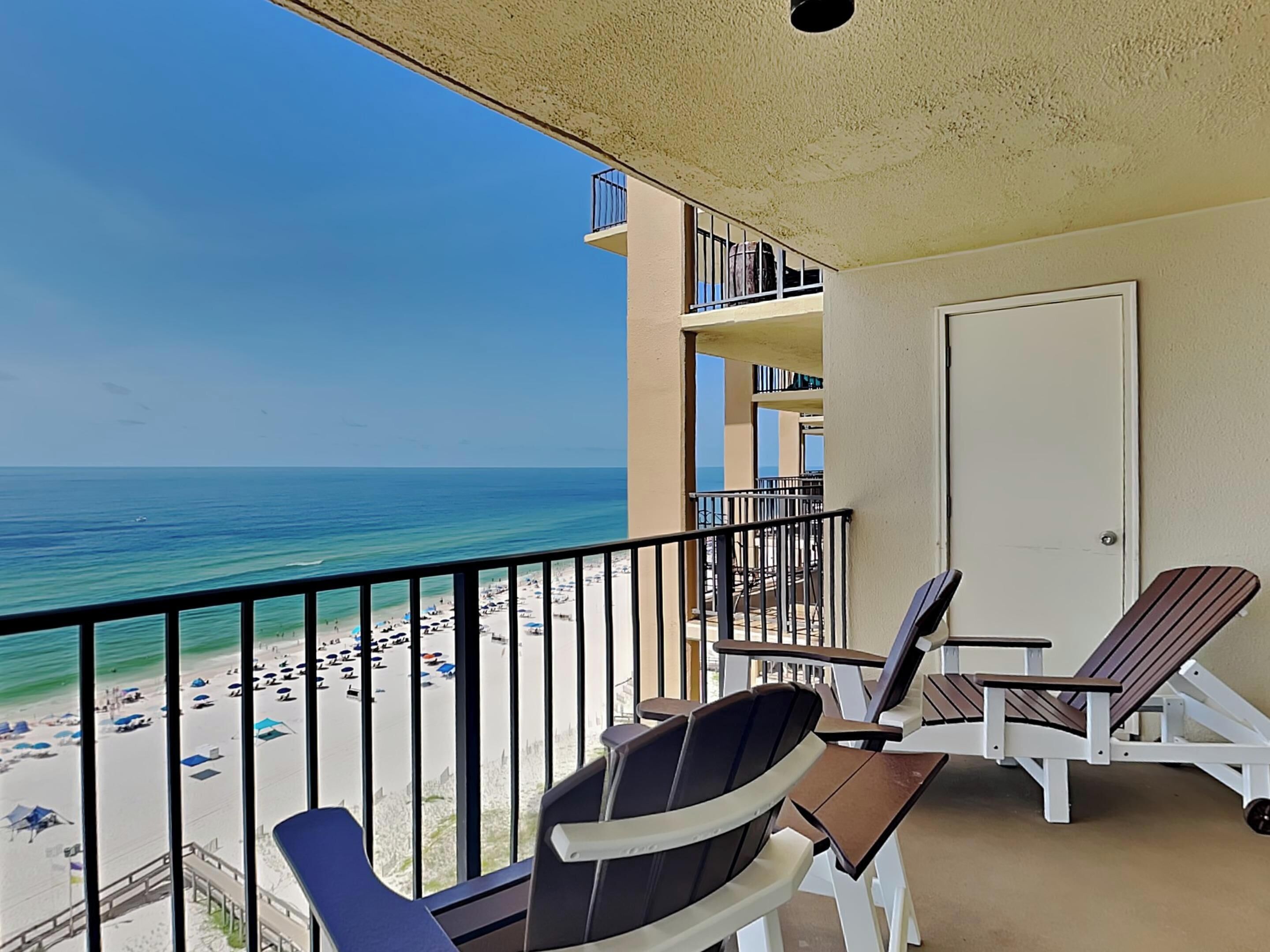 A balcony with a view of the beach and ocean. There are two chairs and a small table.