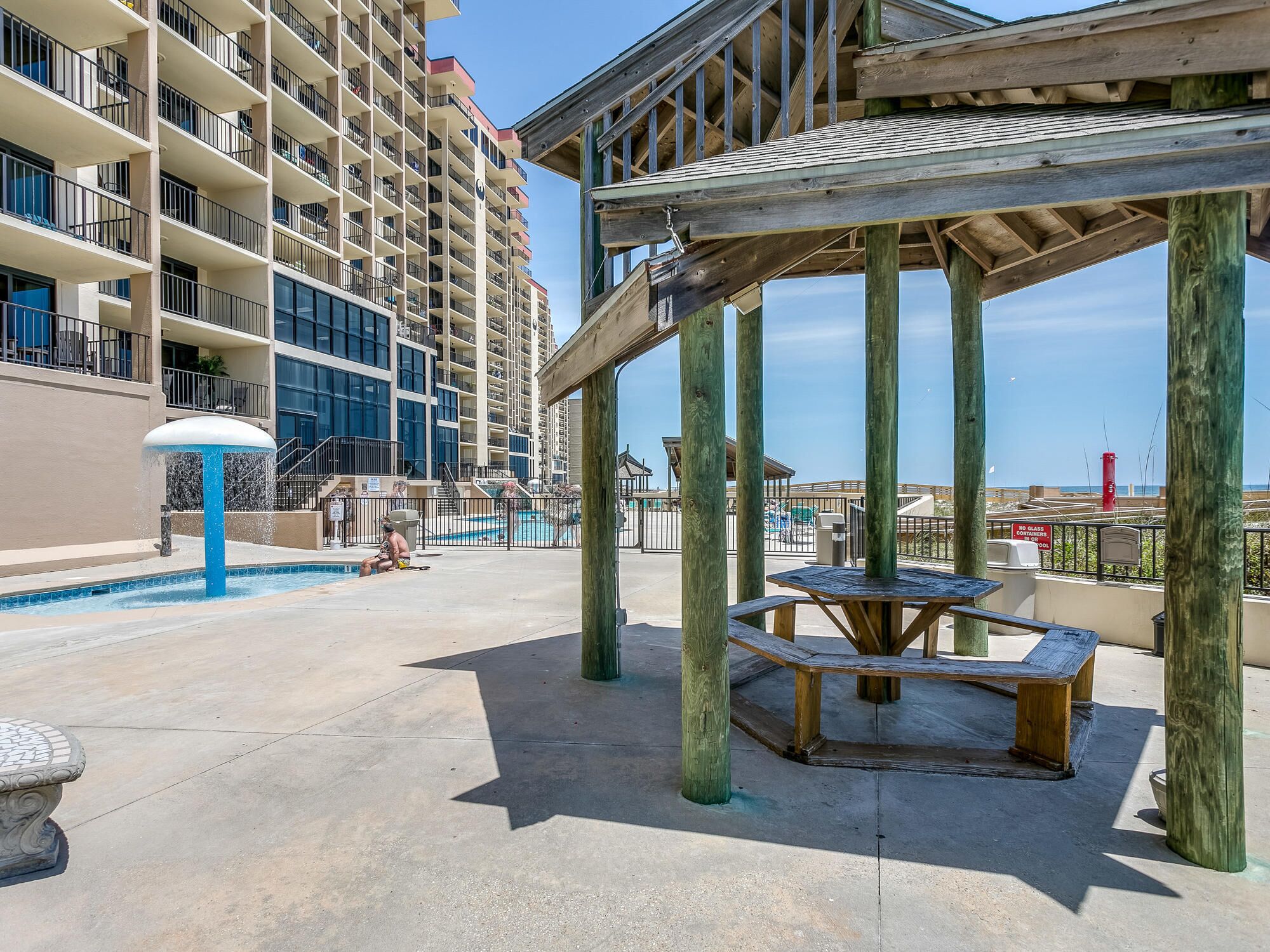 Uma área de piscina com um gazebo de madeira, piscina e um edifício alto ao fundo.