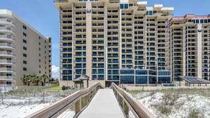 Un hotel moderno de rascacielos con varios balcones, un paseo cubierto y una zona de playa de arena.