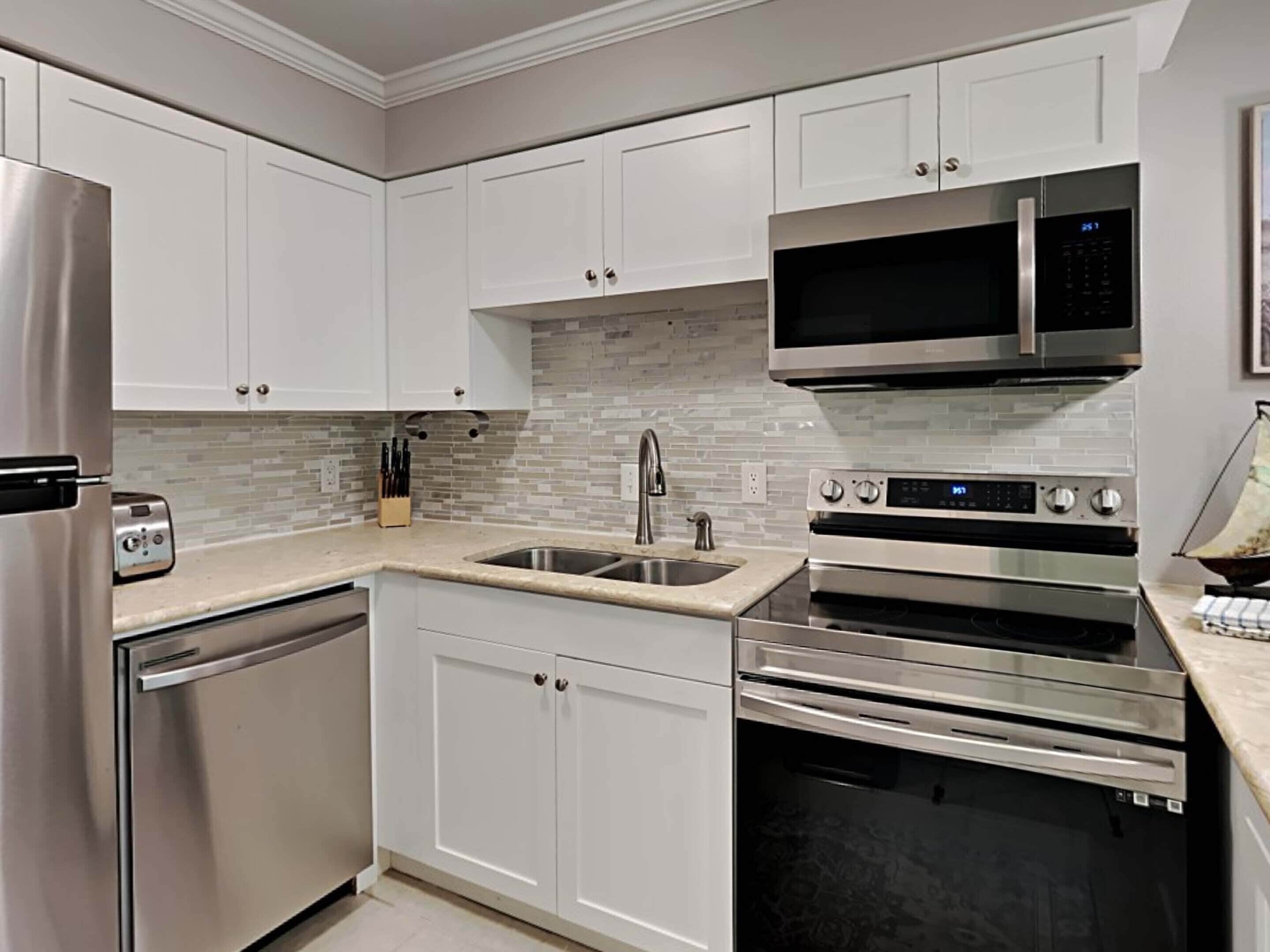 A modern kitchen with white cabinets, a stainless steel refrigerator, a microwave, an oven, and a dishwasher.