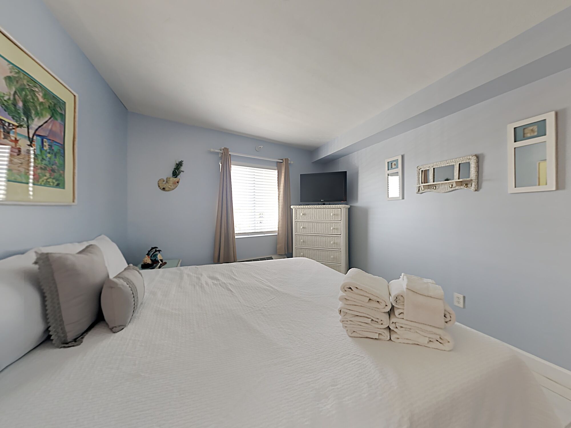 Une chambre à coucher avec un lit, une commode, un téléviseur et une fenêtre avec des rideaux.