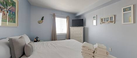 Une chambre à coucher avec un lit, une commode, un téléviseur et une fenêtre avec des rideaux.
