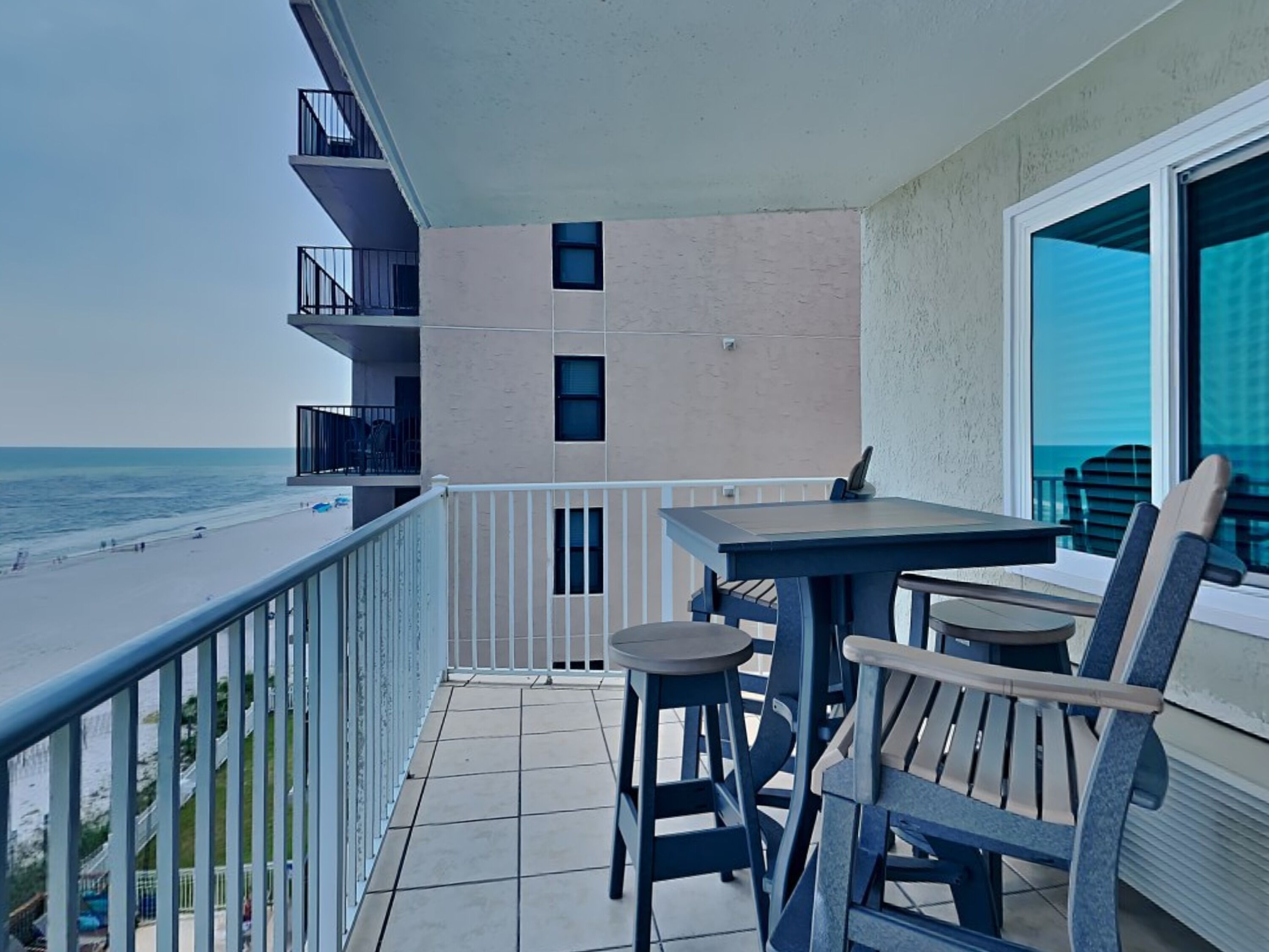 A balcony with a table and chairs, overlooking a beach.