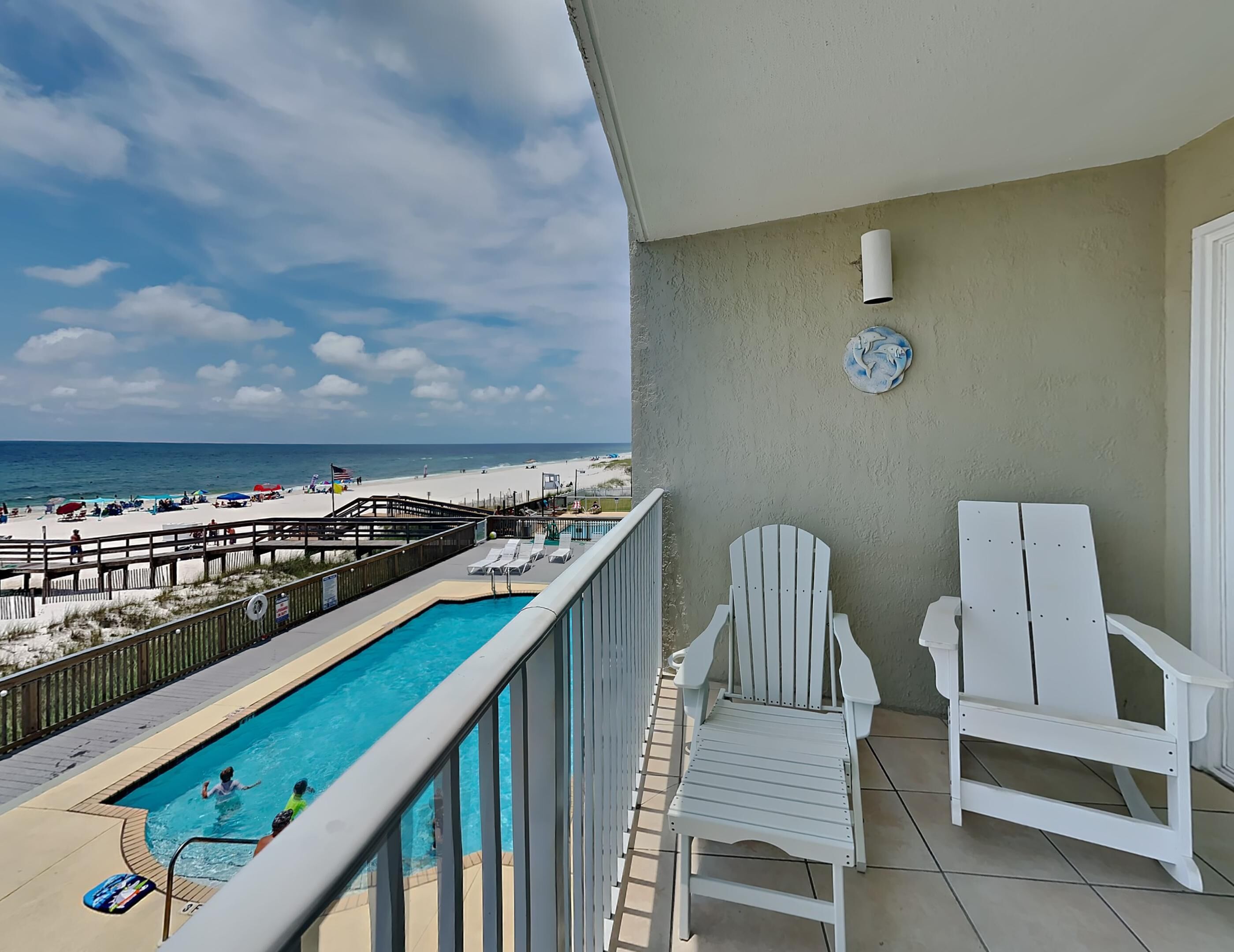 A balcony with a pool, beach view, and white chairs.