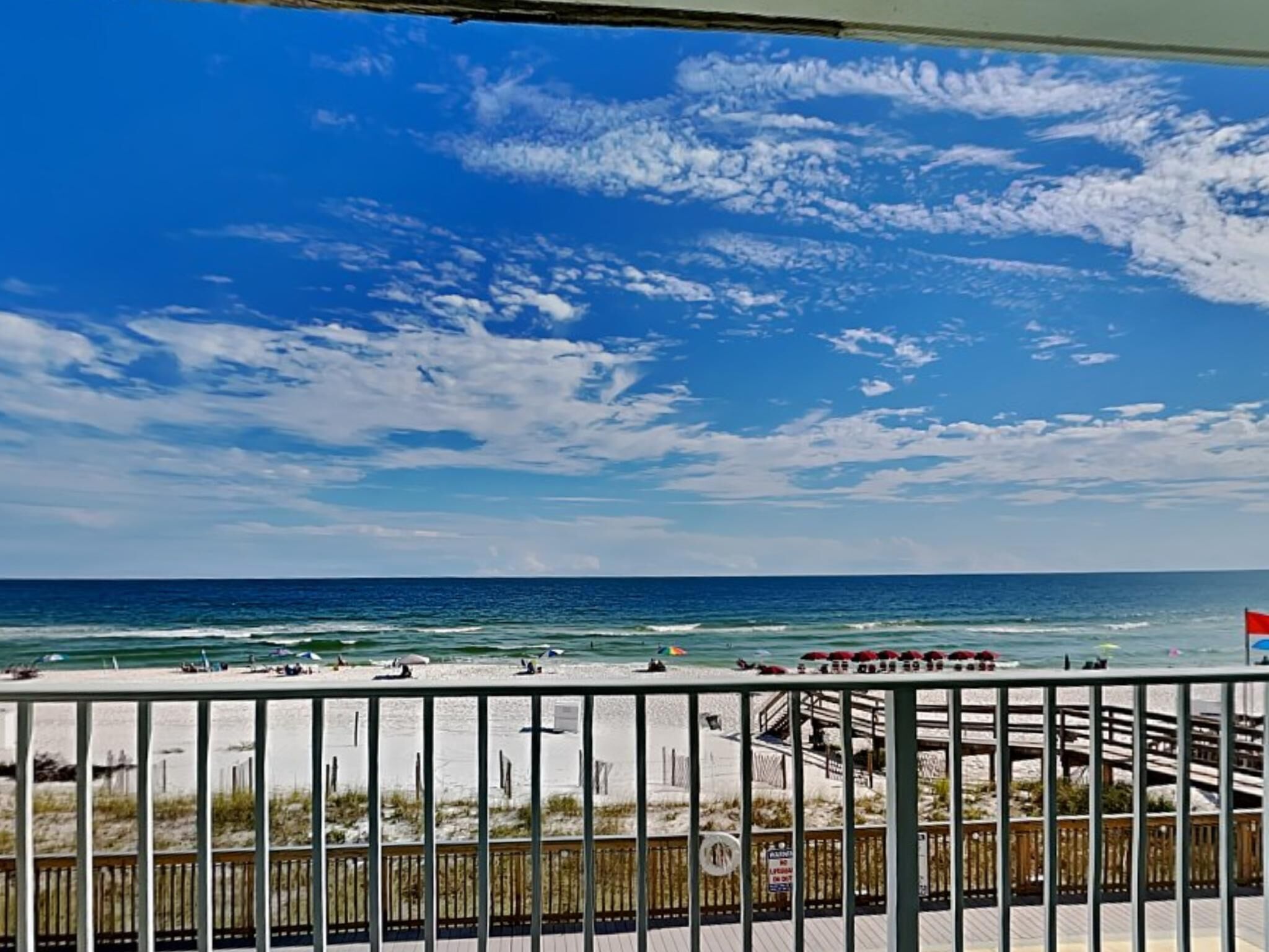Vista a la playa con una terraza de madera y barandilla.