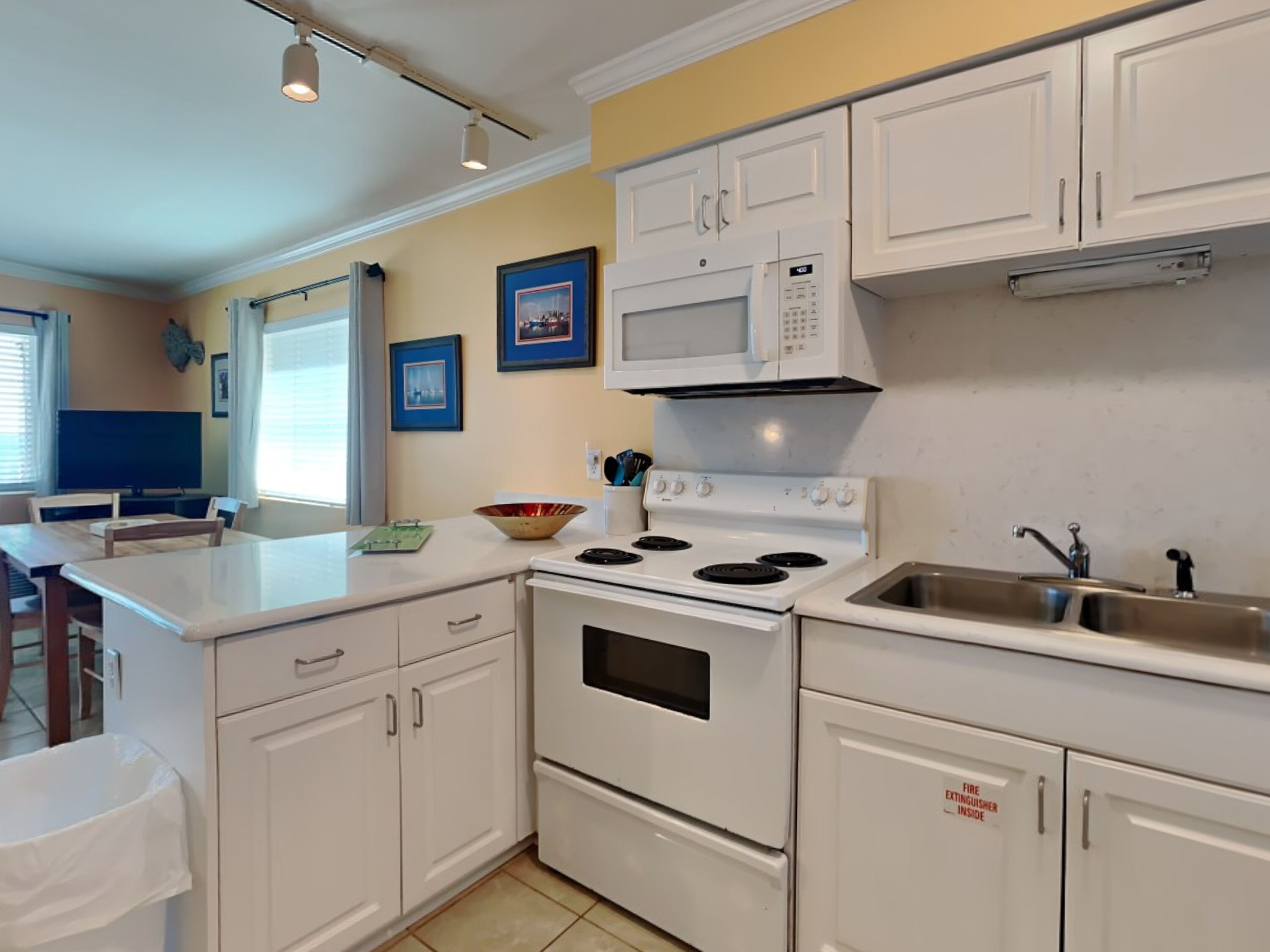 A kitchen with white cabinets, a stove, a microwave, and a sink.