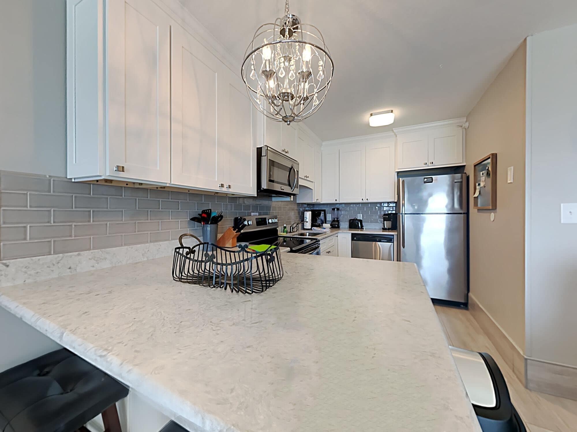 A modern kitchen with white cabinets, a stainless steel refrigerator, a microwave, and a dishwasher.