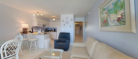A modern living room with a sofa, chairs, a coffee table, and a kitchen in the background.