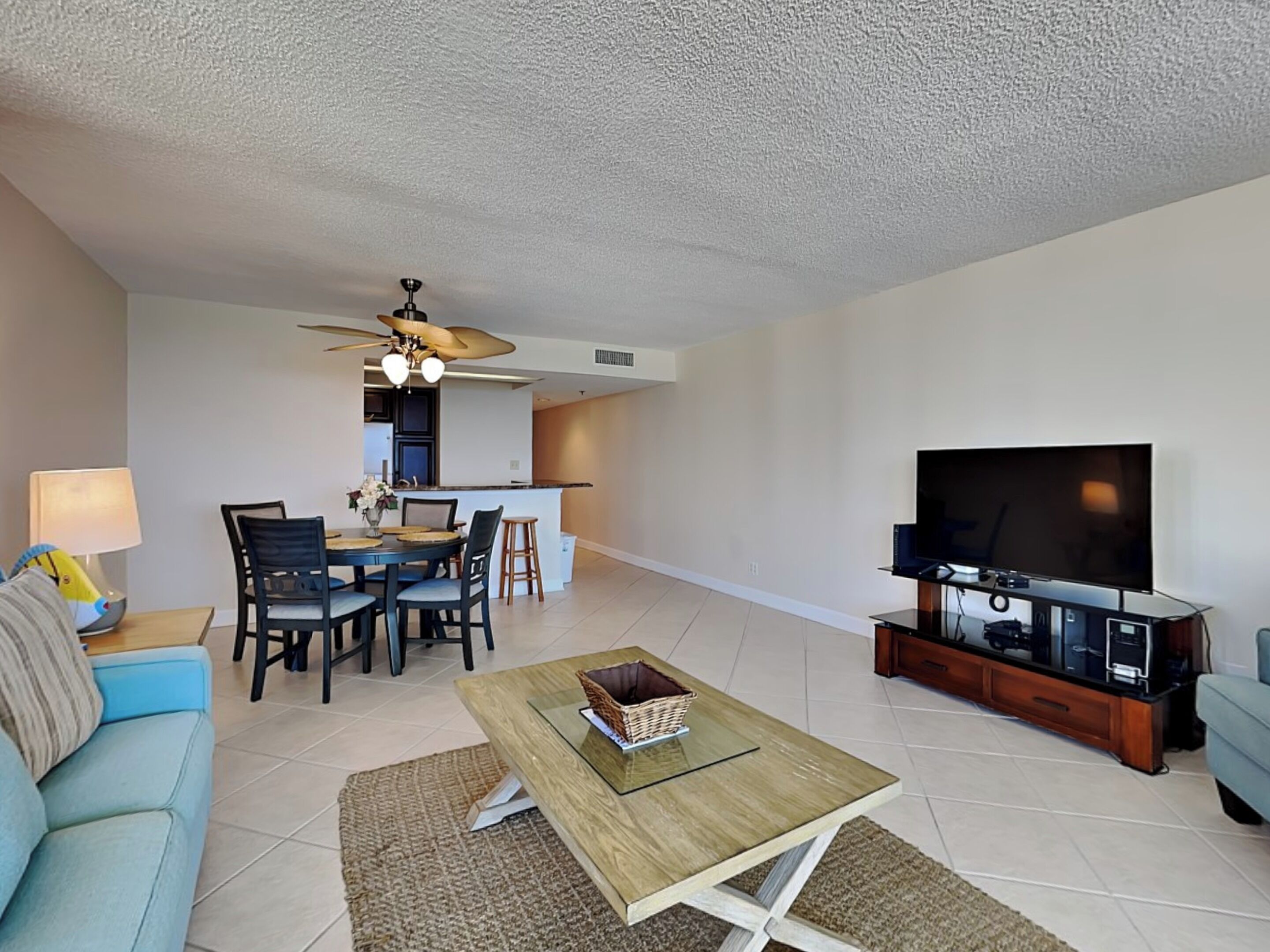 A modern living room with a sofa, coffee table, TV, and a dining area with chairs and a kitchen in the background.