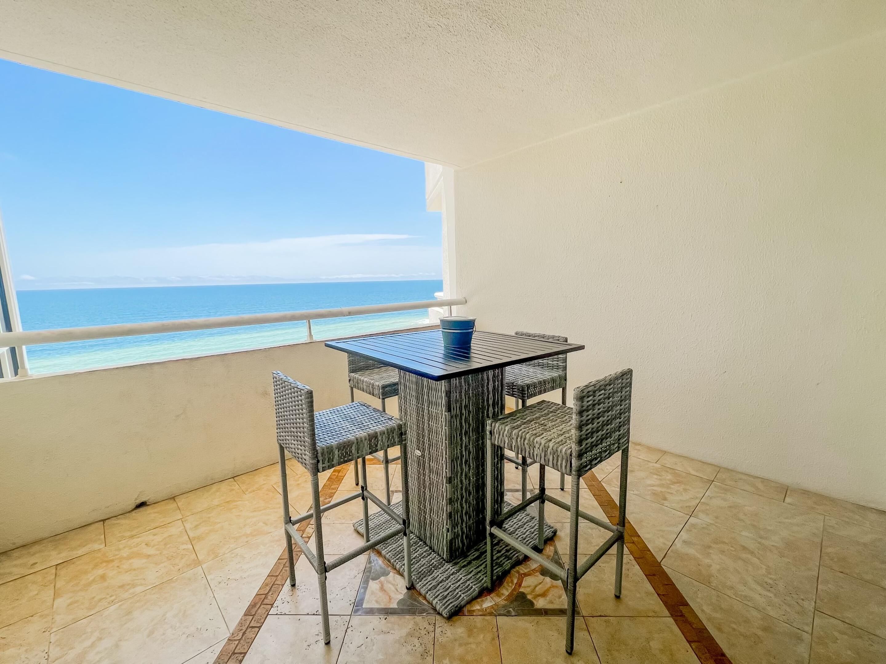 A balcony with a table and chairs, overlooking a beach.
