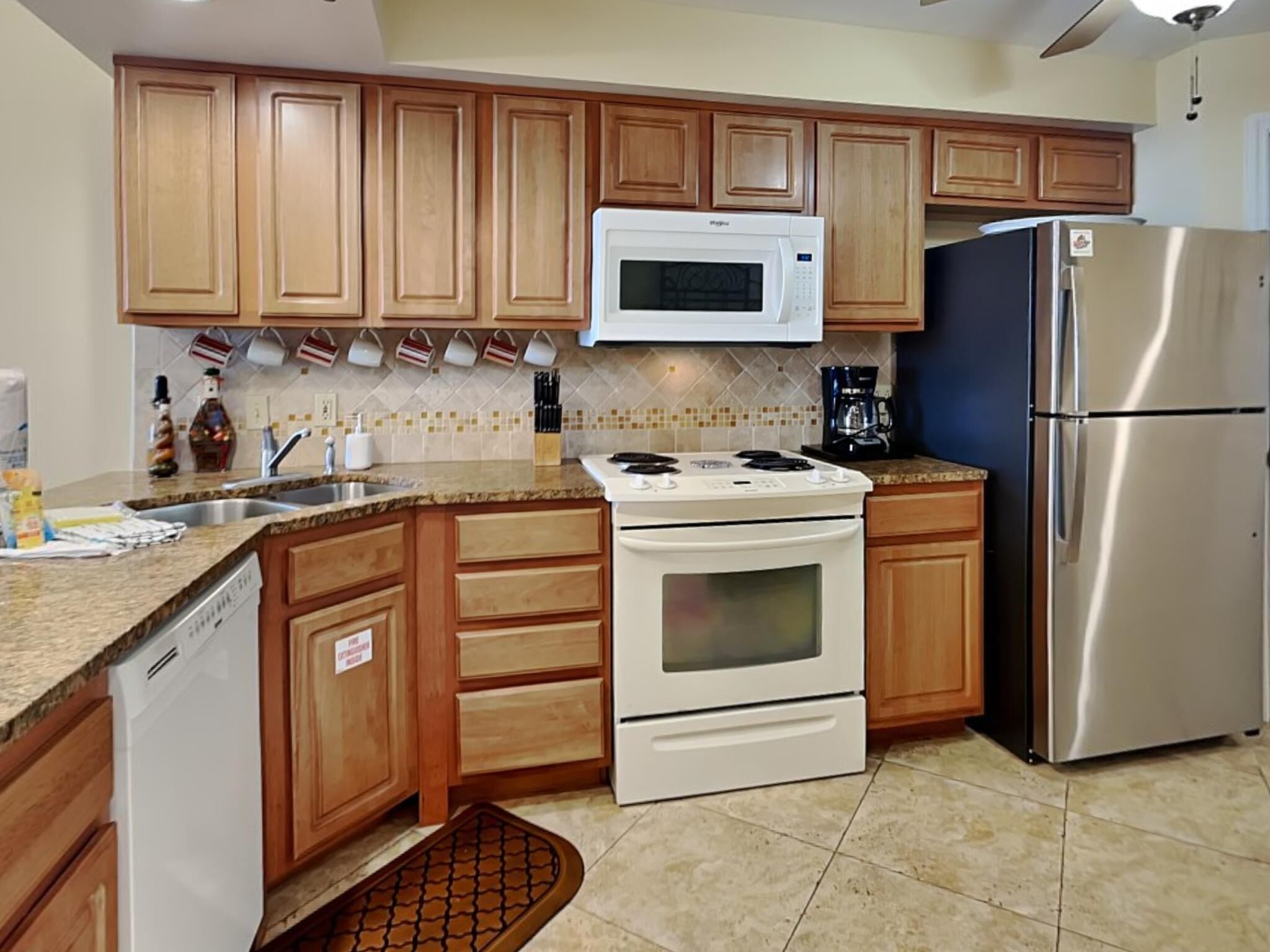 A kitchen with wooden cabinets, a white microwave, a stainless steel refrigerator, a stove, and a coffee maker.