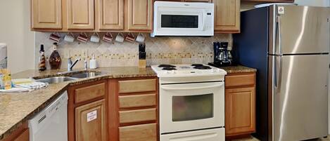 A kitchen with wooden cabinets, a white microwave, a stainless steel refrigerator, a stove, and a coffee maker.