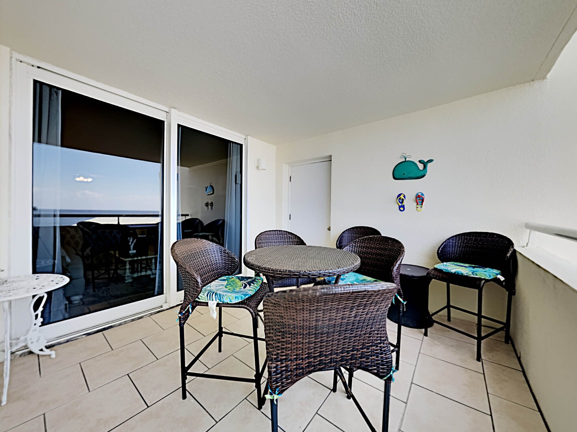 A balcony with wicker furniture, a glass door leading to a pool, and a view of the sea.