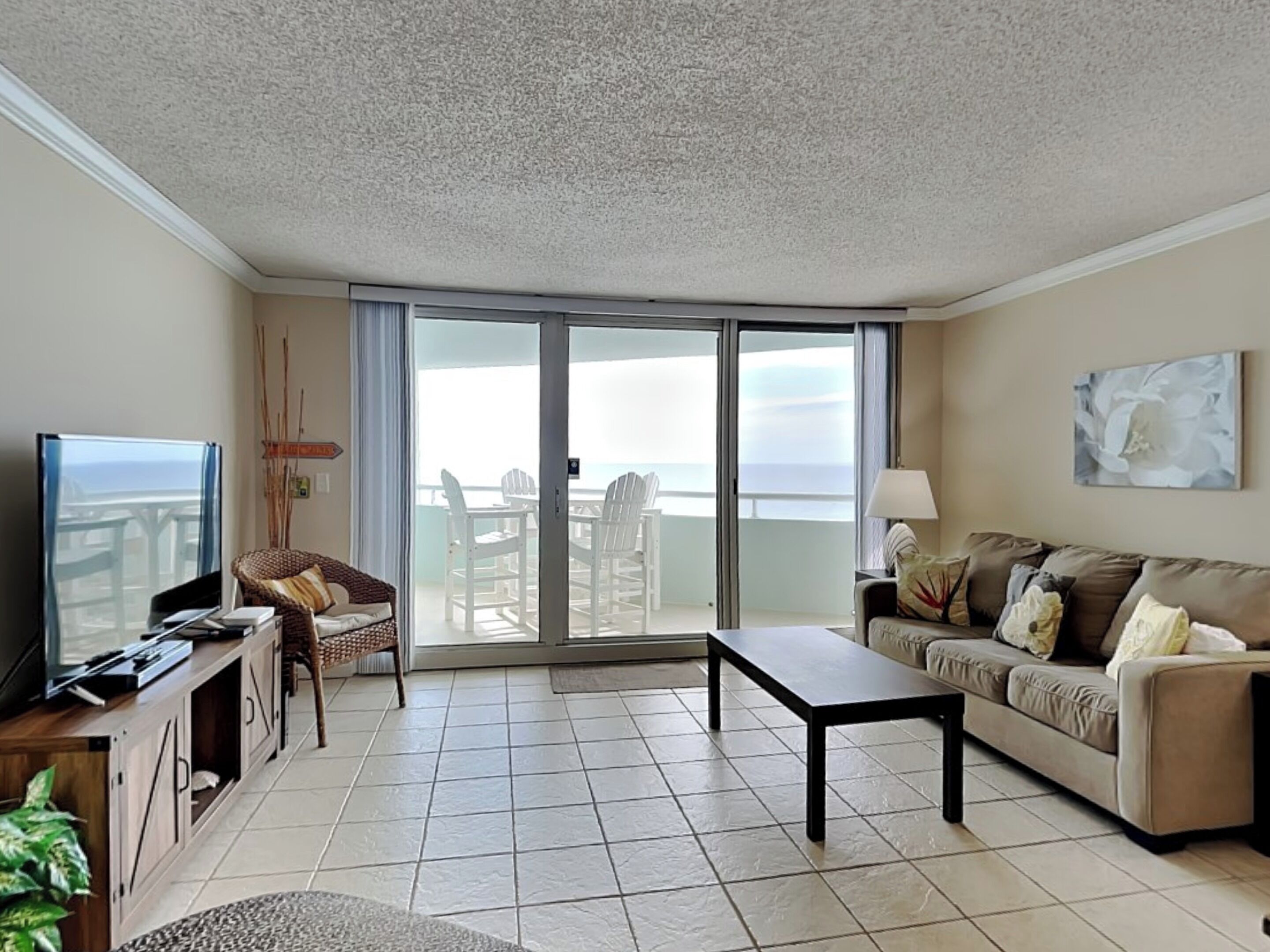 A spacious living room with a large sliding glass door leading to a balcony with a view of the ocean.