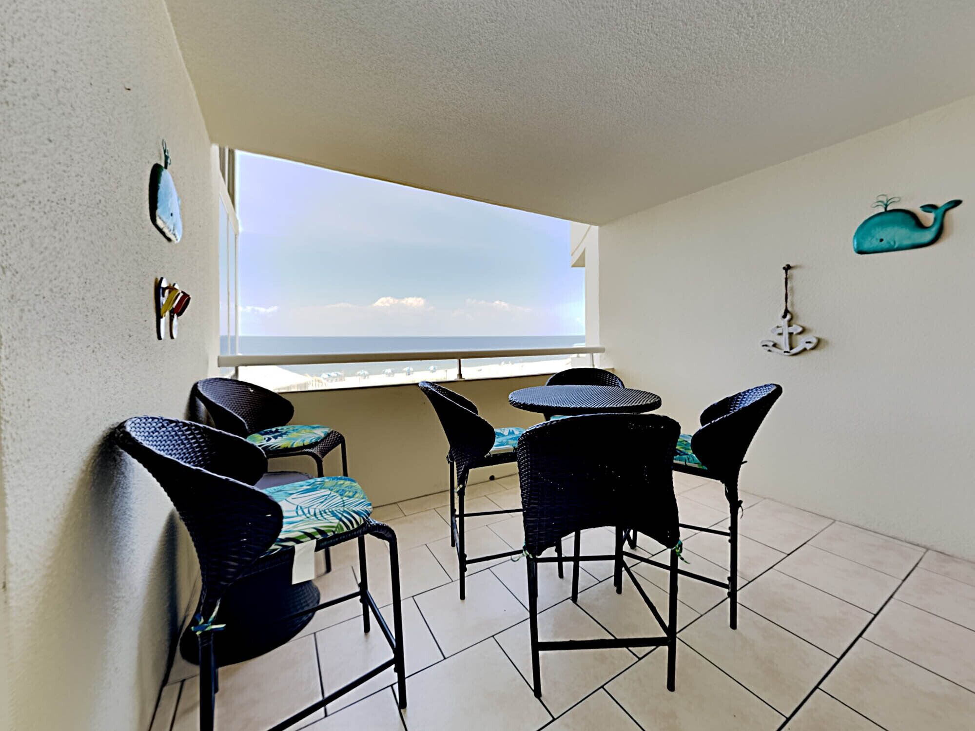 A balcony with four chairs and a table, a window overlooking the sea, and nautical decor including a whale and anchor.