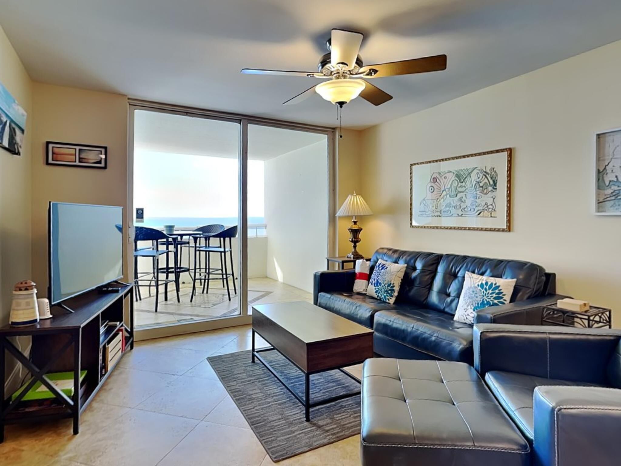 A modern living room with a flat-screen TV, a leather sofa, a coffee table, and a ceiling fan.
