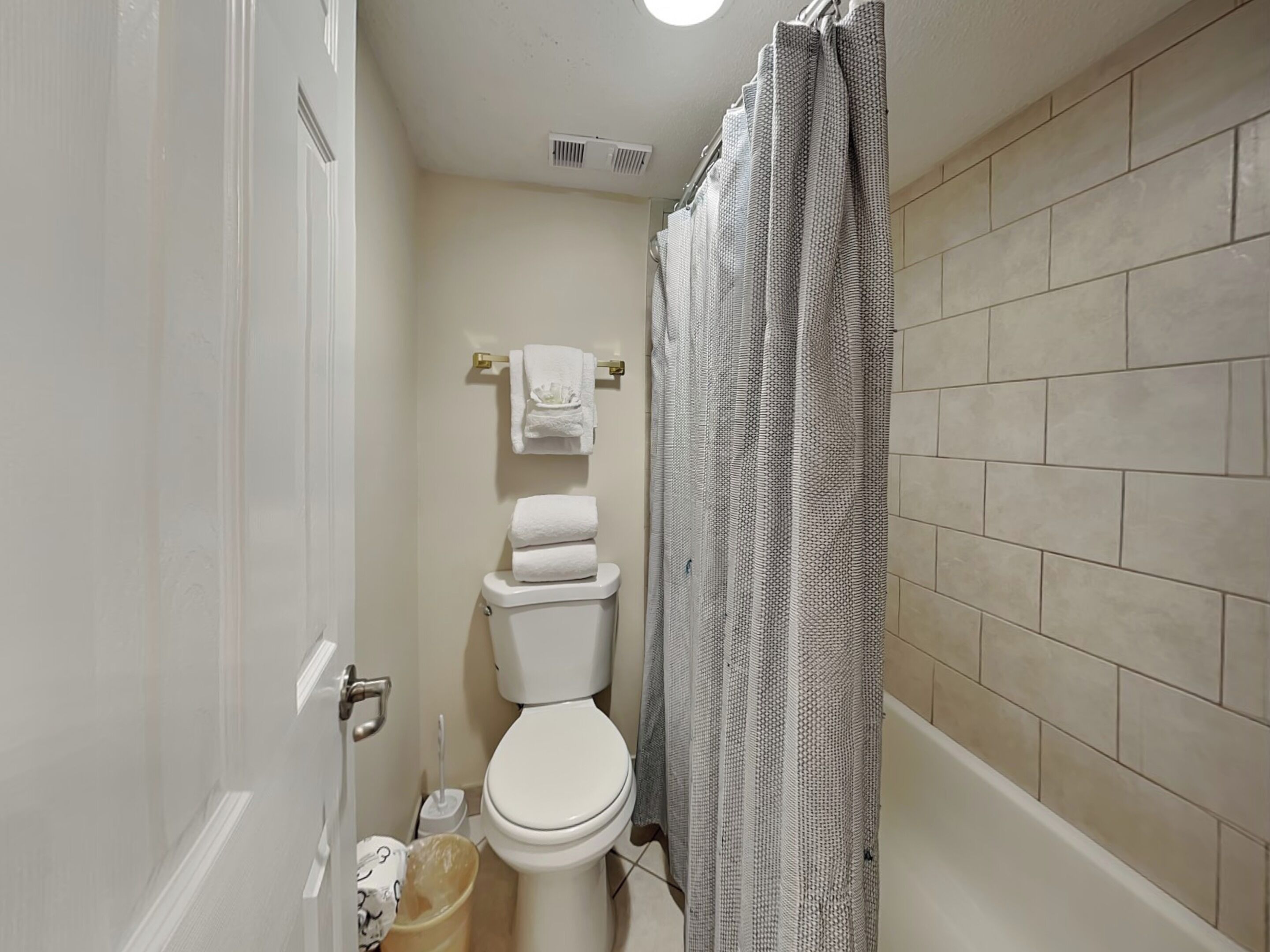 A small bathroom with a toilet, a shower curtain, and a tiled wall.
