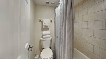 A small bathroom with a toilet, a shower curtain, and a tiled wall.