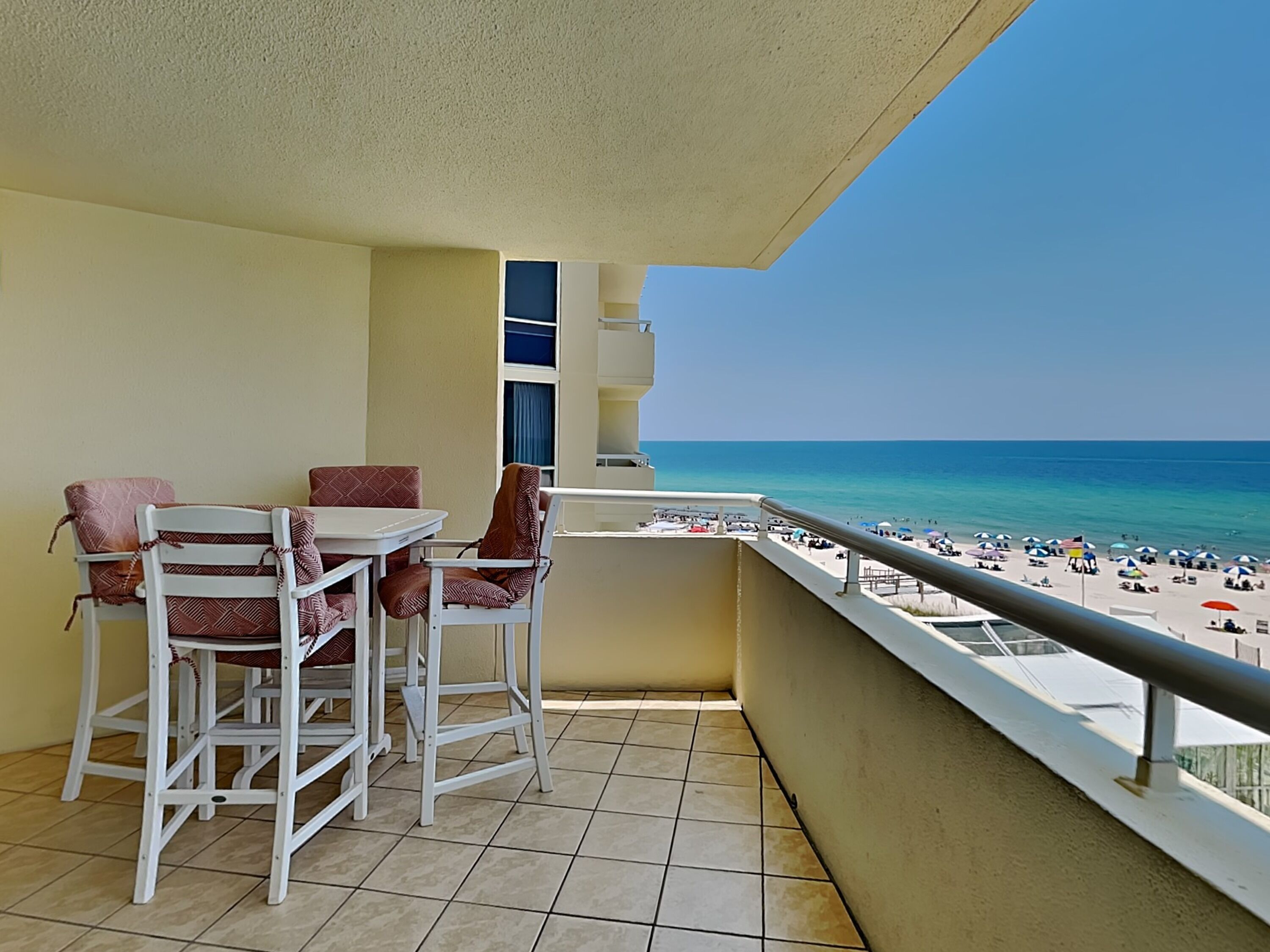 Un balcón con vista a la playa, muebles blancos y suelo de baldosas.