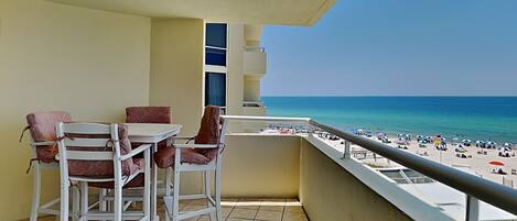 Un balcón con vista a la playa, muebles blancos y suelo de baldosas.