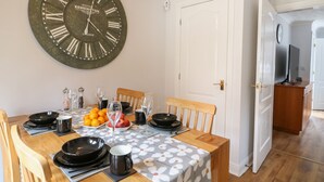 A dining area with a large wall clock, a table set for four with plates, glasses, and a fruit bowl.