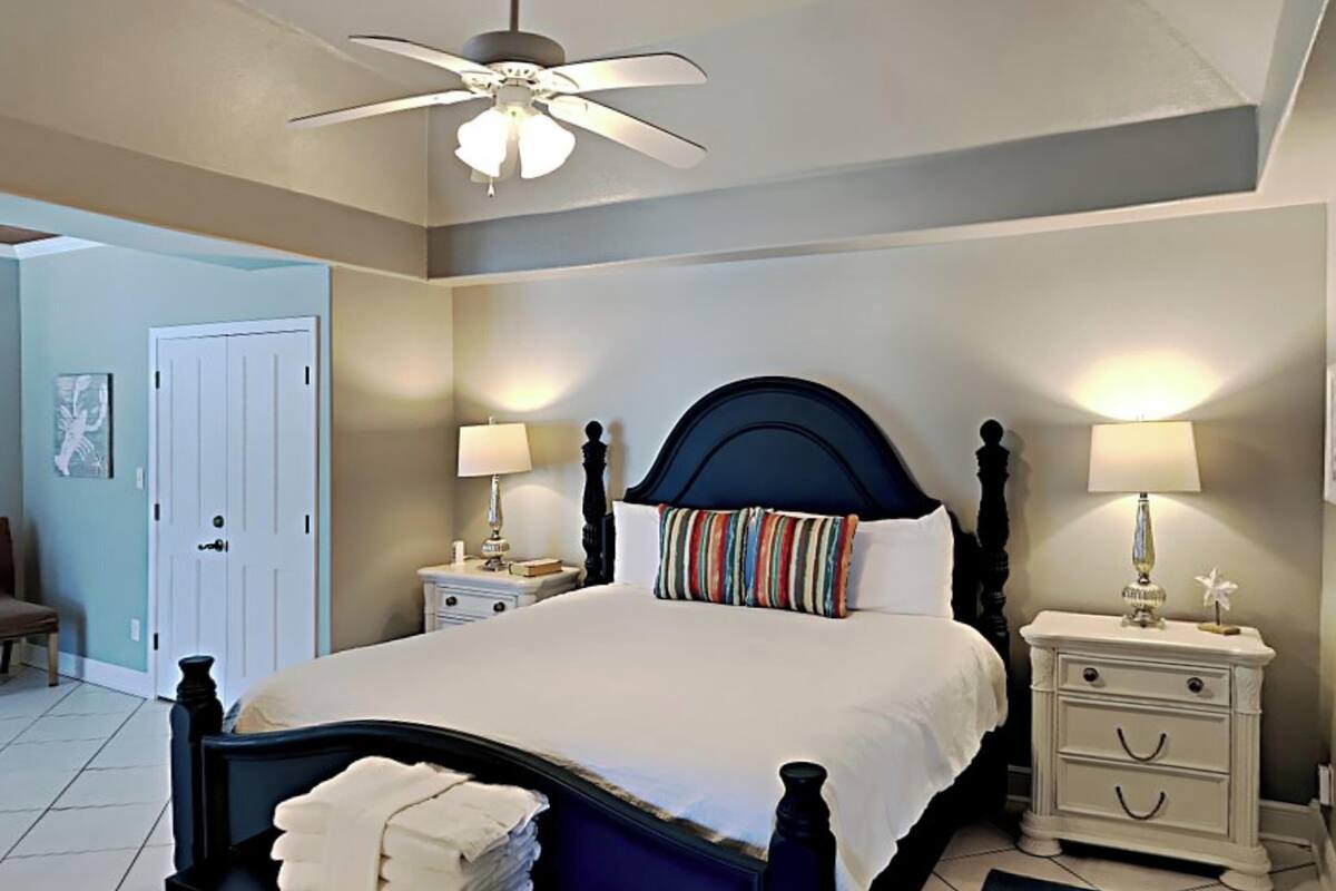 A neatly arranged bedroom with a bed, bedside tables, a ceiling fan, and a door.