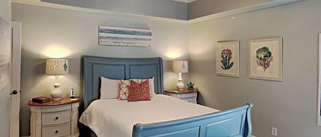 A bedroom with a bed, bedside tables, a bench, a ceiling fan, and artwork on the walls.