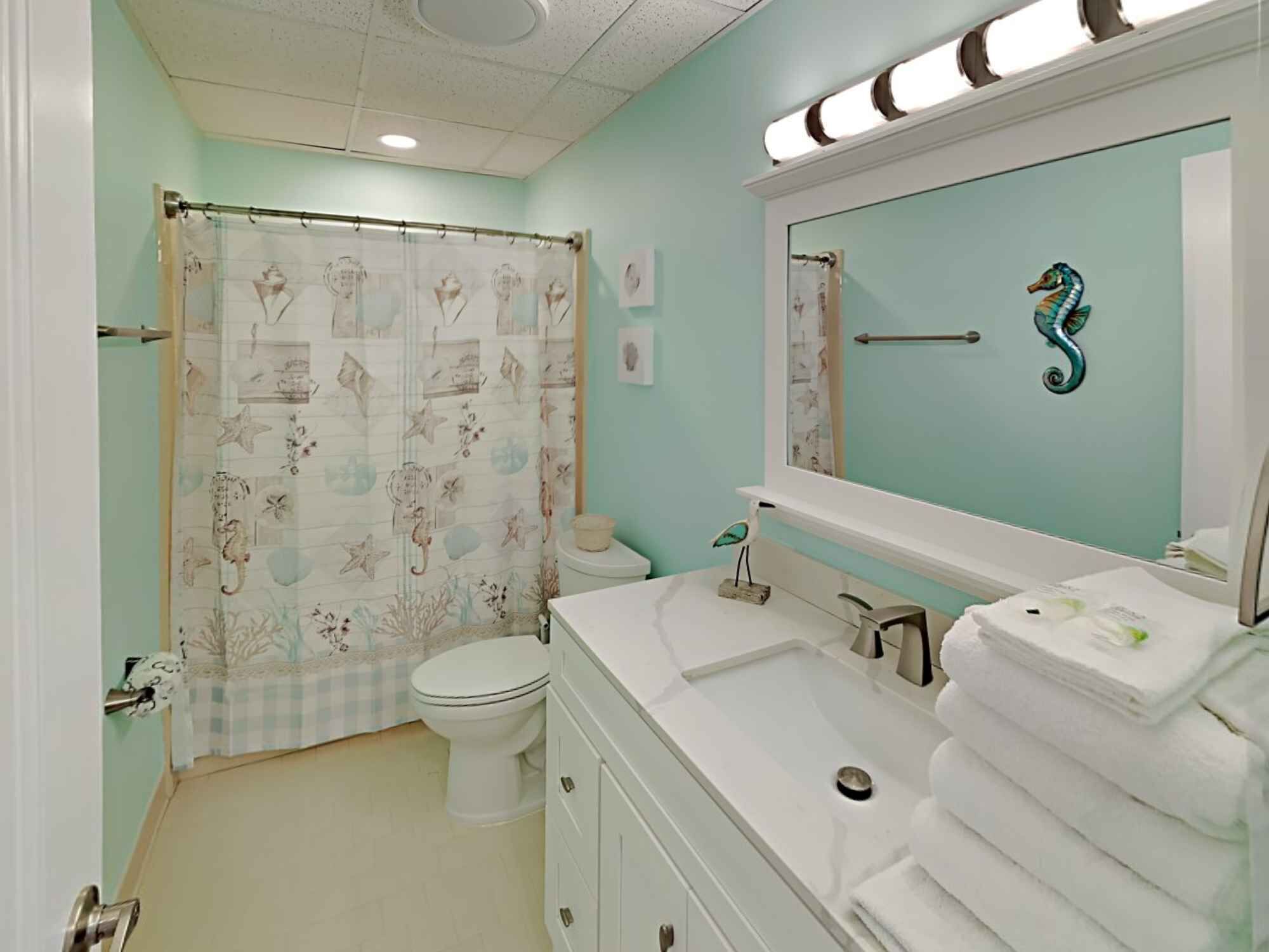 A bathroom with a seahorse mirror, a toilet, and a sink with stacked towels.